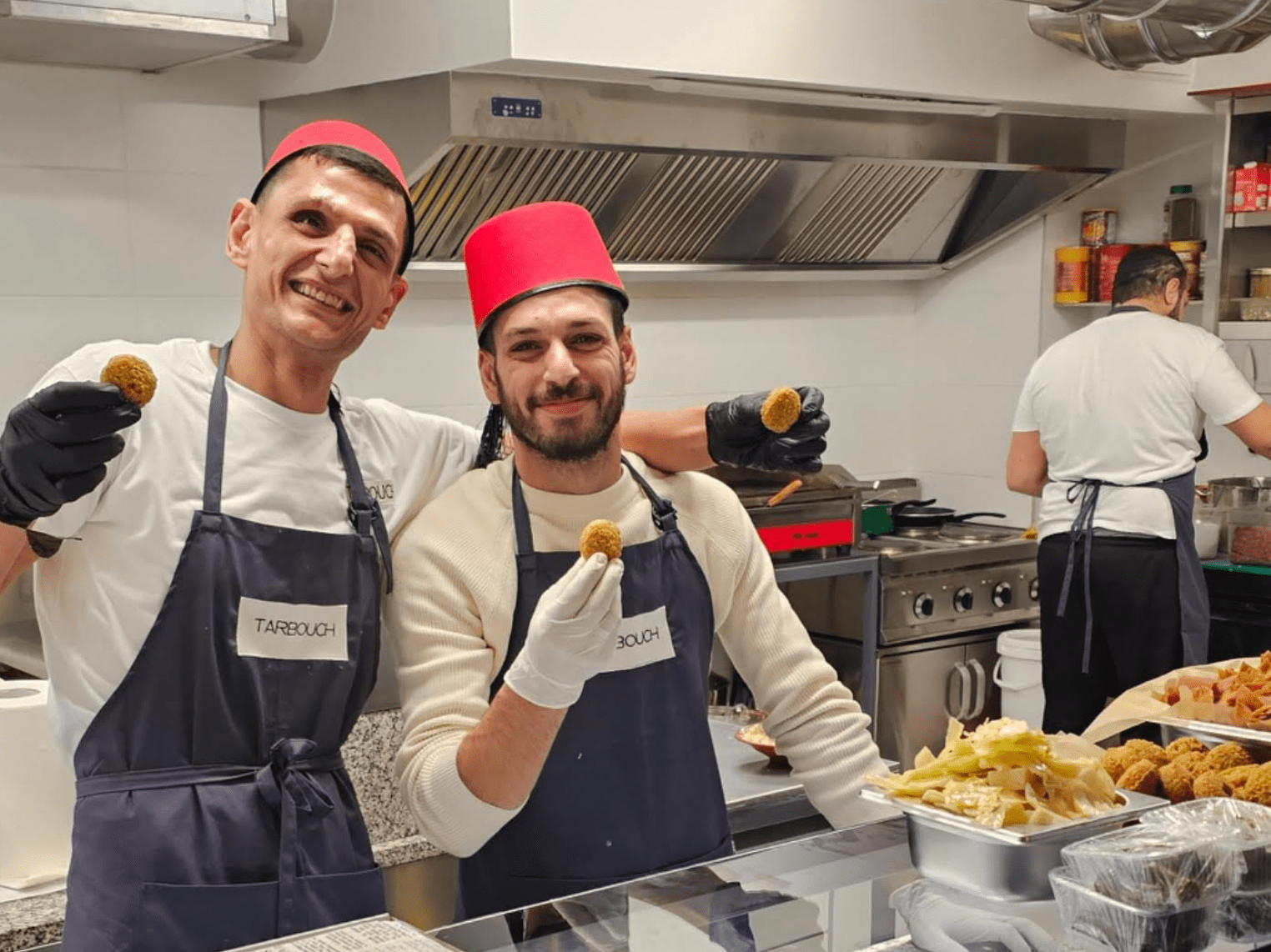 photo de Tarek Kahraman chef et de son équipe souriants dans leur cuisine et tenant des pièces de Falafel dans la main pour accueillir les clients